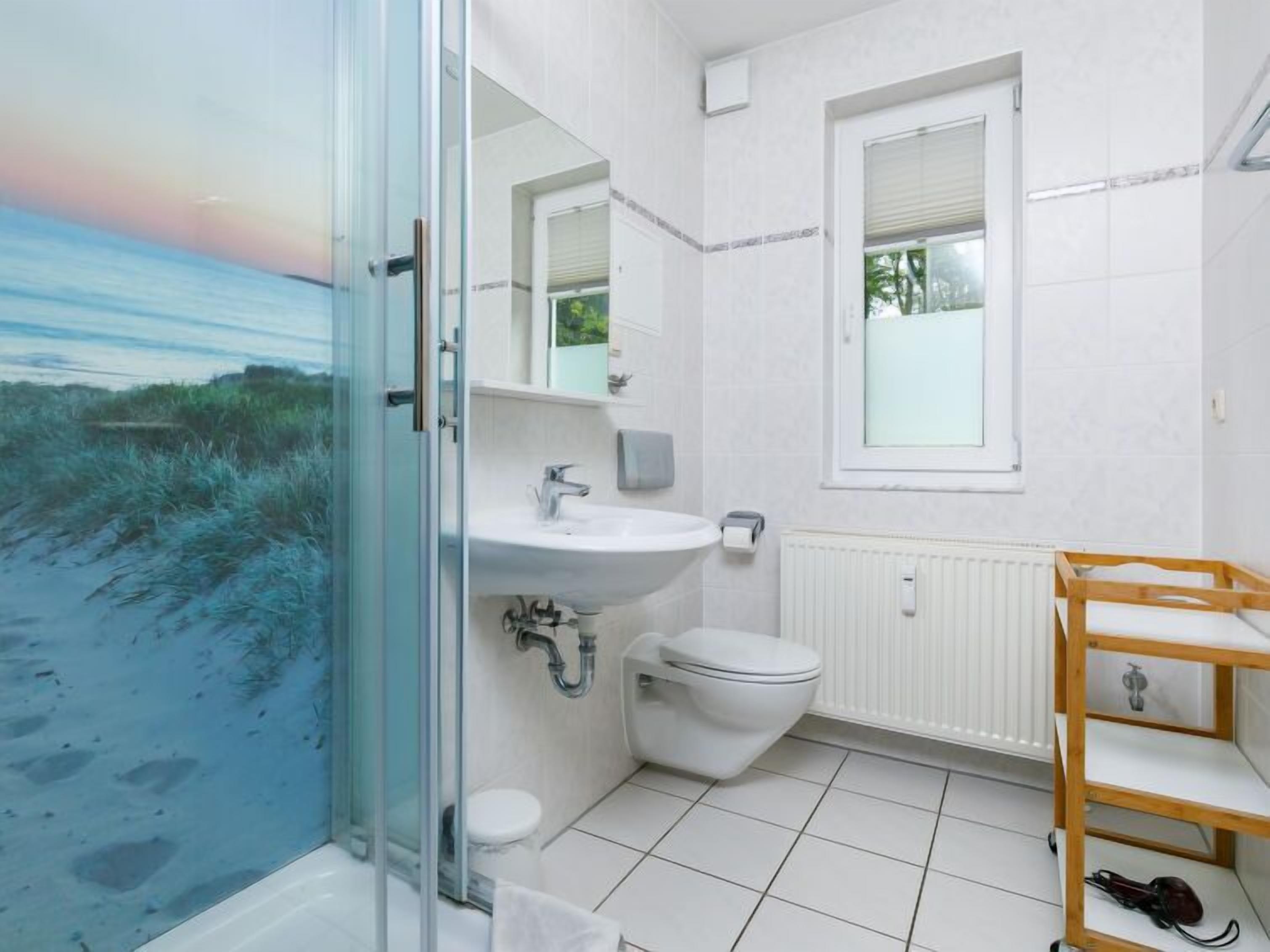 Un bany amb plat de dutxa de vidre, un lavabo, un vàter i una finestra.