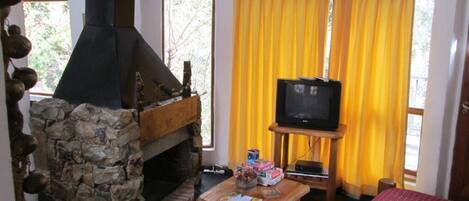 A room with a stone fireplace, a television on a stand, and a bed with a red cover.