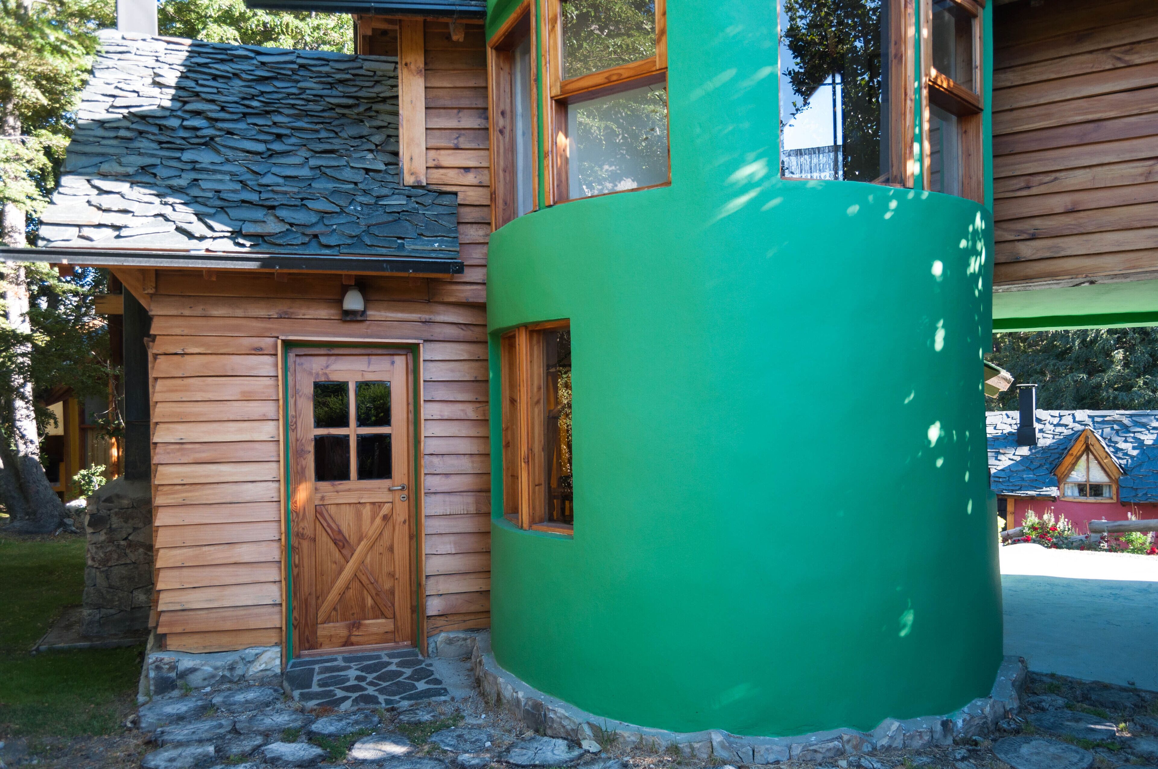 Une cabane en bois avec une structure cylindrique verte, des fondations en pierre et une porte en bois.