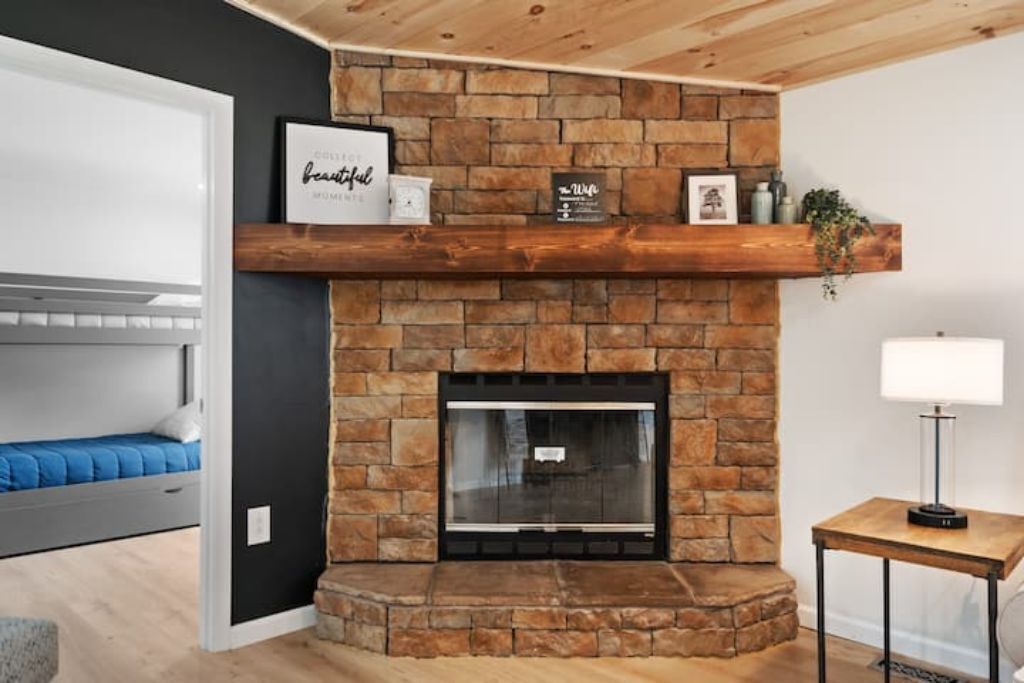 A modern living room with a stone fireplace, a wooden ceiling, and a bed with blue bedding.