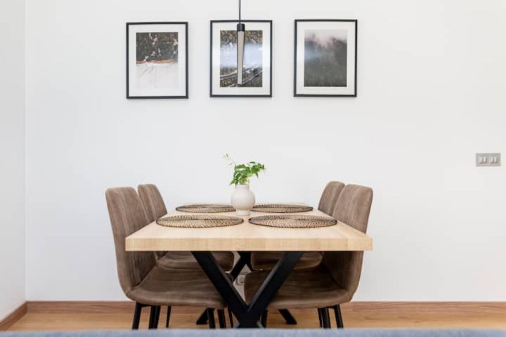 Una mesa de comedor con cuatro sillas, un florero con una planta y tres cuadros en la pared.