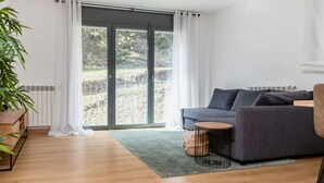 Ett modernt vardagsrum med en grå soffa, ett litet runt bord och en stor skjutdörr i glas som leder ut till ett utomhusområde.