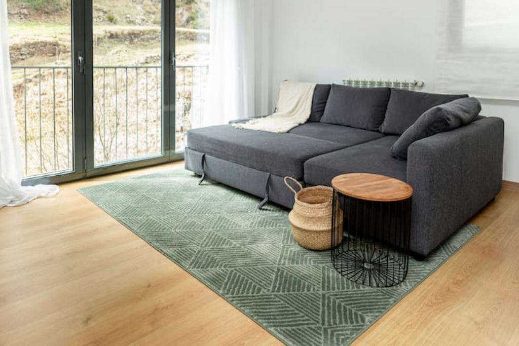 A modern living room with a grey sectional sofa, a green patterned rug, and a wooden side table.