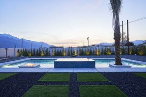 A rectangular pool with a built-in fire feature, surrounded by a landscaped garden with a palm tree, and a backdrop of mountains.