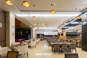 A spacious indoor area with multiple tables and chairs, overhead lighting fixtures, and a visible kitchen area in the background. - Howard Johnson Puhui Plaza Chongqing Qijiang (Chongqing)