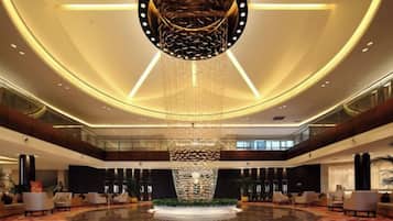 Un hall espacioso con una gran araña central, varias zonas de estar y una alfombra circular grande.