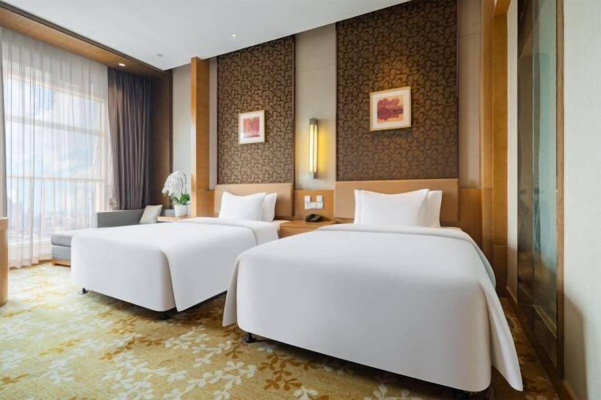 Ein Hotelzimmer mit zwei Betten, einem Schreibtisch und einem großen Fenster mit Vorhängen.