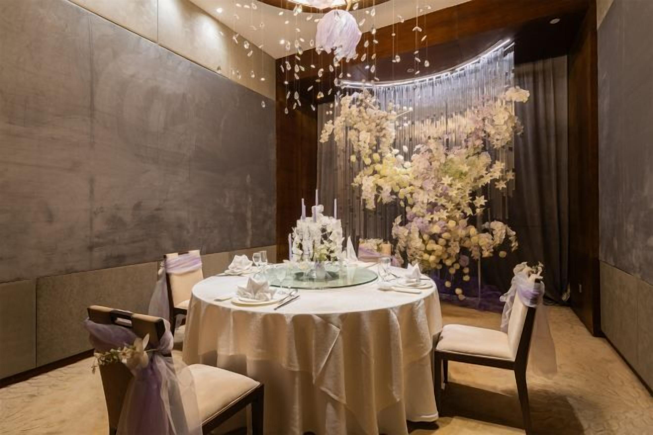 A round dining table with a white tablecloth, surrounded by chairs, in a room with a modern interior design.