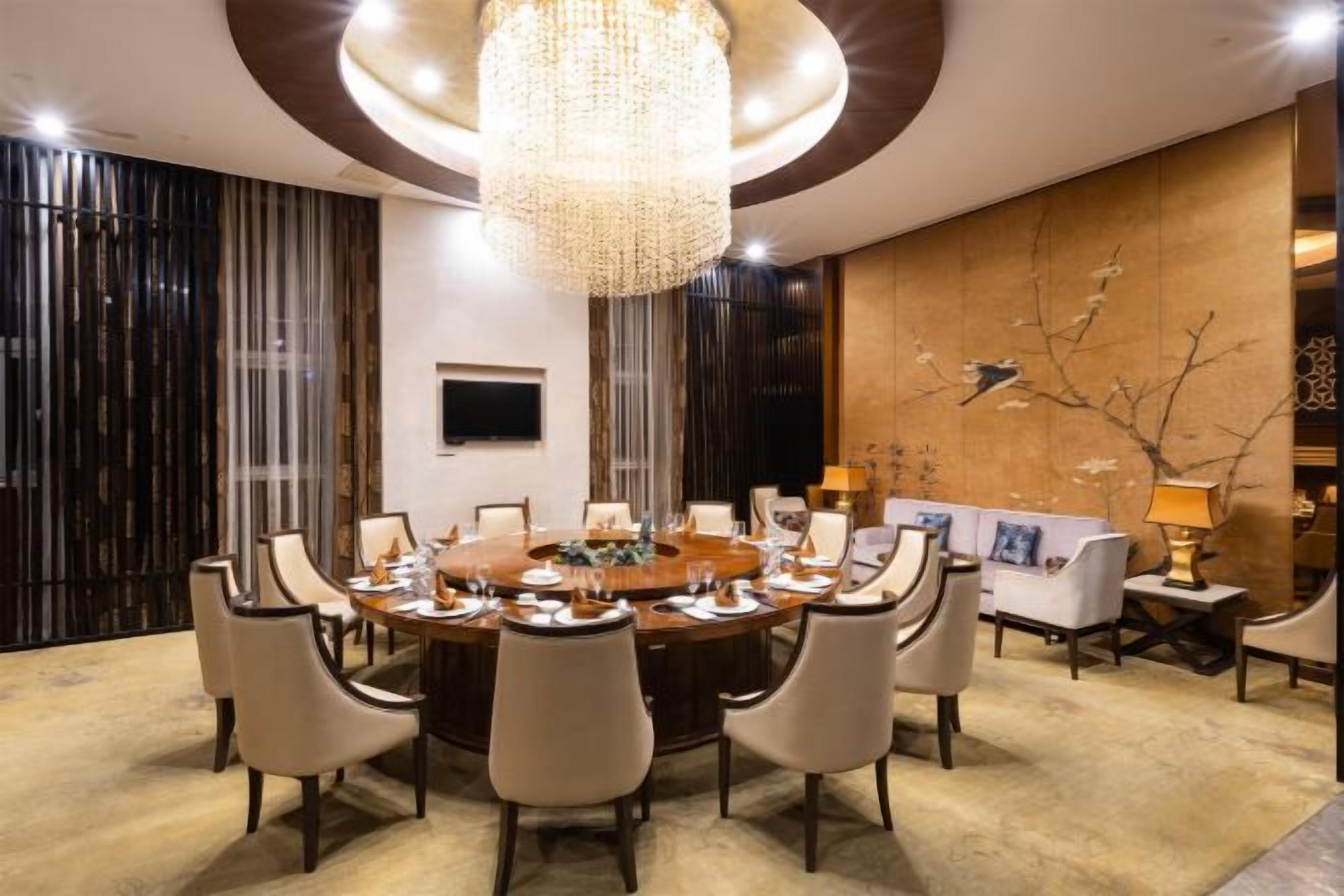 Un comedor formal con una mesa redonda, sillas, una araña y un televisor en la pared.