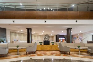 Un vestíbulo de hotel con mostrador de recepción, zona de estar y barandilla de cristal que domina el espacio.