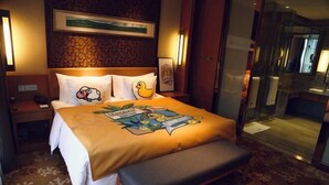A hotel room with a bed featuring cartoon character pillows, a bench, a framed picture on the wall, and a carpeted floor.