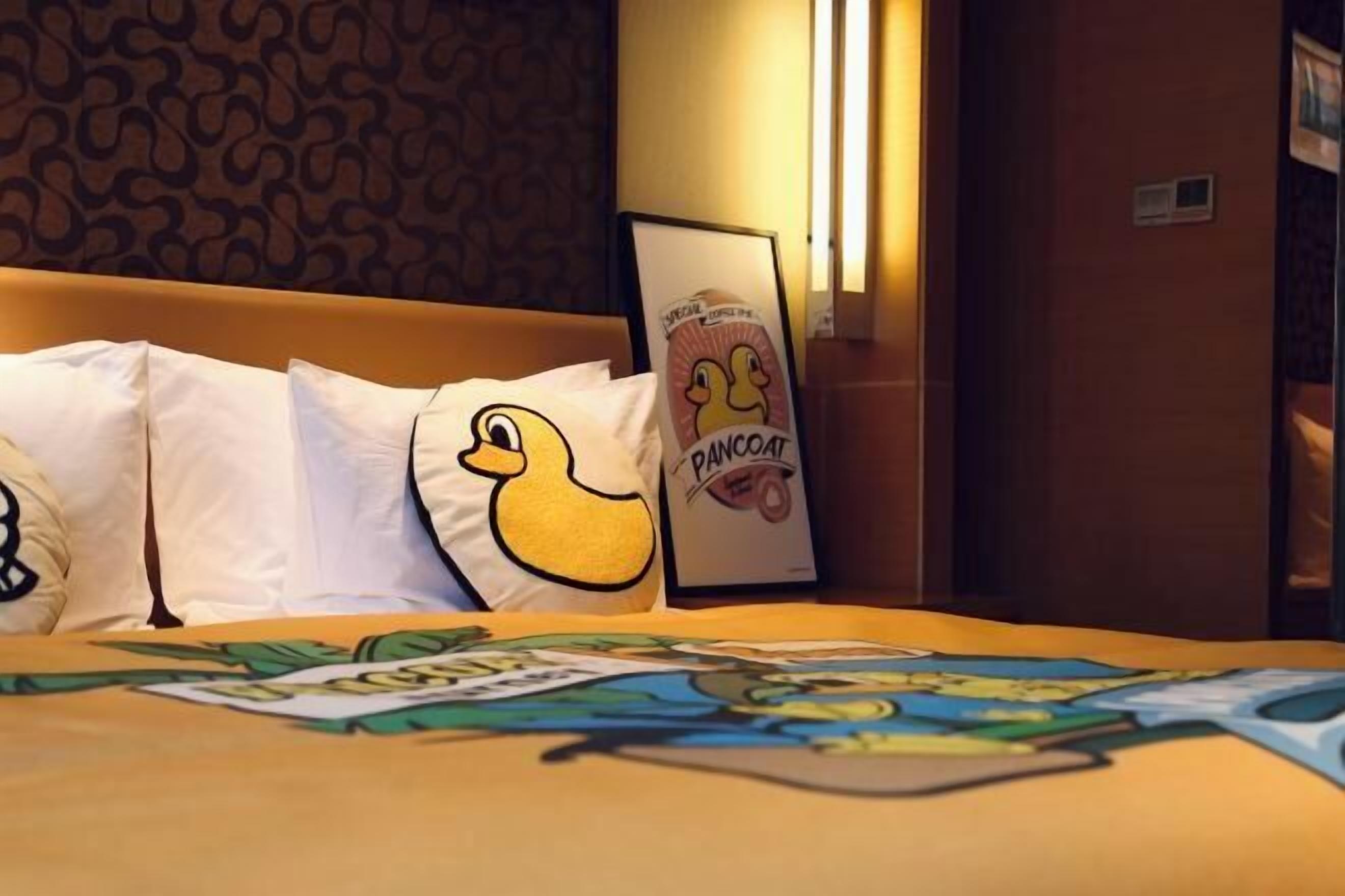 Una habitación de hotel con una cama, un almohadón de pato y un cuadro enmarcado con un pato.