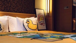 A hotel room with a bed featuring a duck pillow and a framed picture of a duck.
