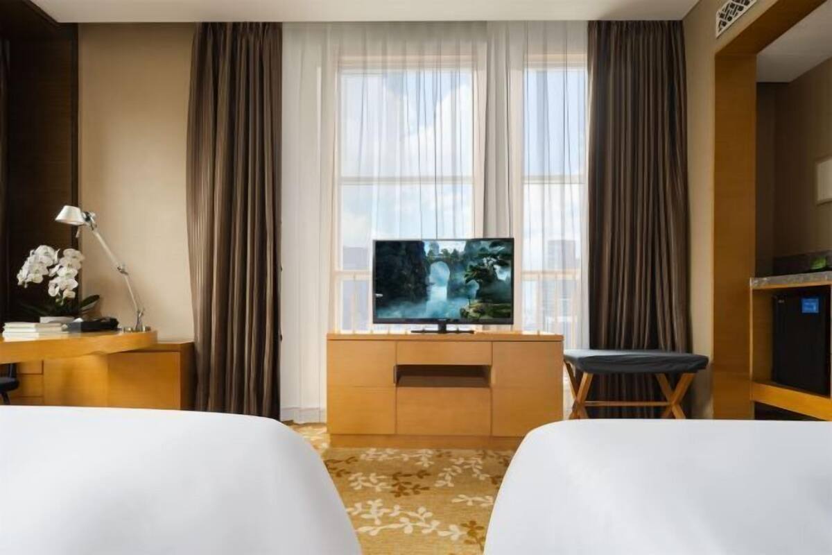 Ein Hotelzimmer mit zwei Betten, einem Fernseher auf einem Holzständer, einem Schreibtisch mit Lampe und Blick auf einen Wasserfall durch das Fenster.