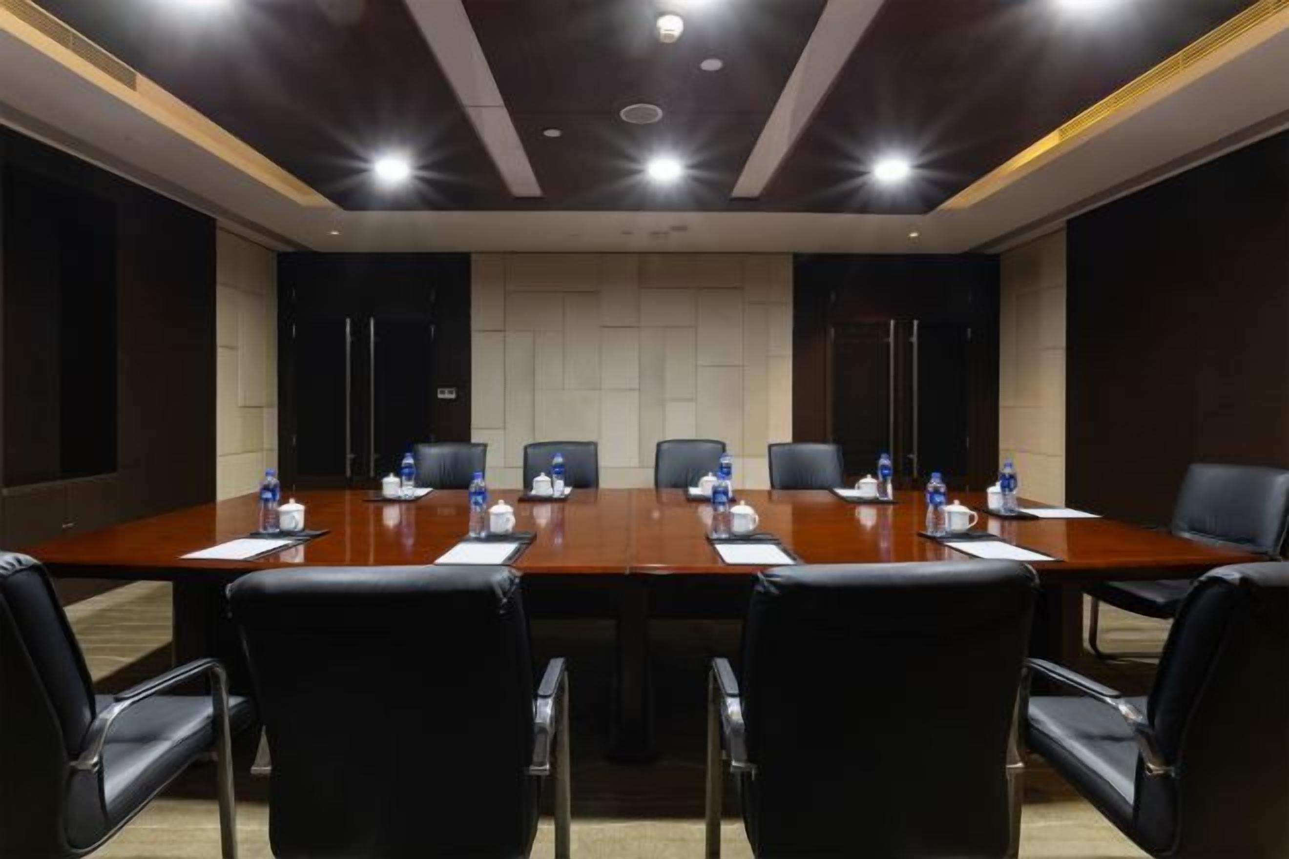 Un salón de conferencias con una larga mesa, sillas negras y botellas de agua.