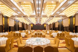 A banquet hall with round tables and chairs, a stage at the front, and a high ceiling with lights. - Howard Johnson Puhui Plaza Chongqing Qijiang (Chongqing)