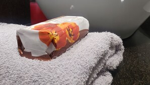 Un baño con un lavamanos blanco, un dispensador de jabón de vidrio y una toalla con estampado floral.