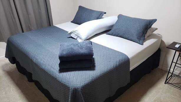 Una cama bien hecha con una colcha azul, almohadas y una toalla doblada al lado.