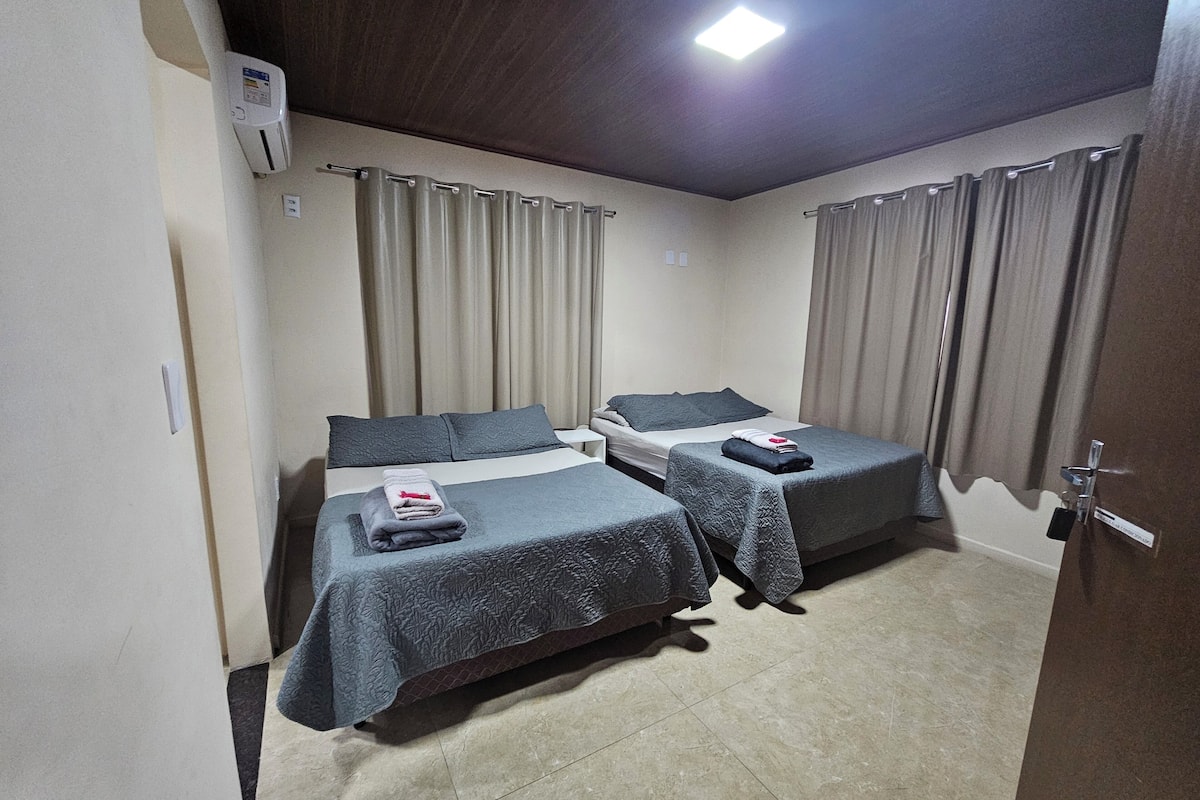 Quarto de hotel com duas camas, uma mesa de cabeceira e uma luminária no teto.