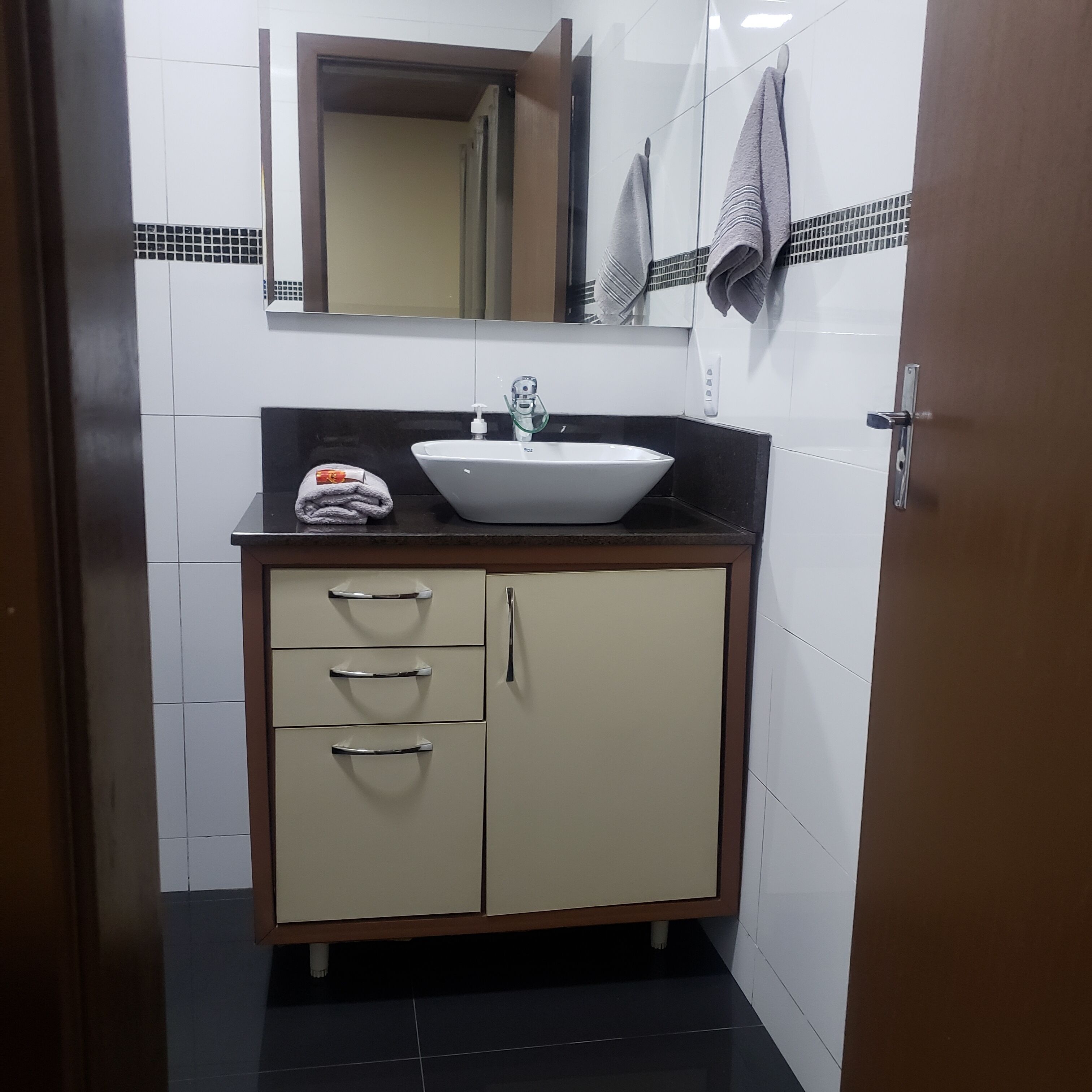 Un baño con lavamanos blanco, un espejo y un perchero para toallas.