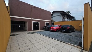 Un estacionamiento con tres coches, un edificio de fachada marrón y una entrada con portón.