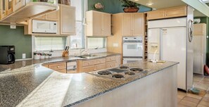 A kitchen with granite countertops, a central island with a stove, a refrigerator, and a microwave.