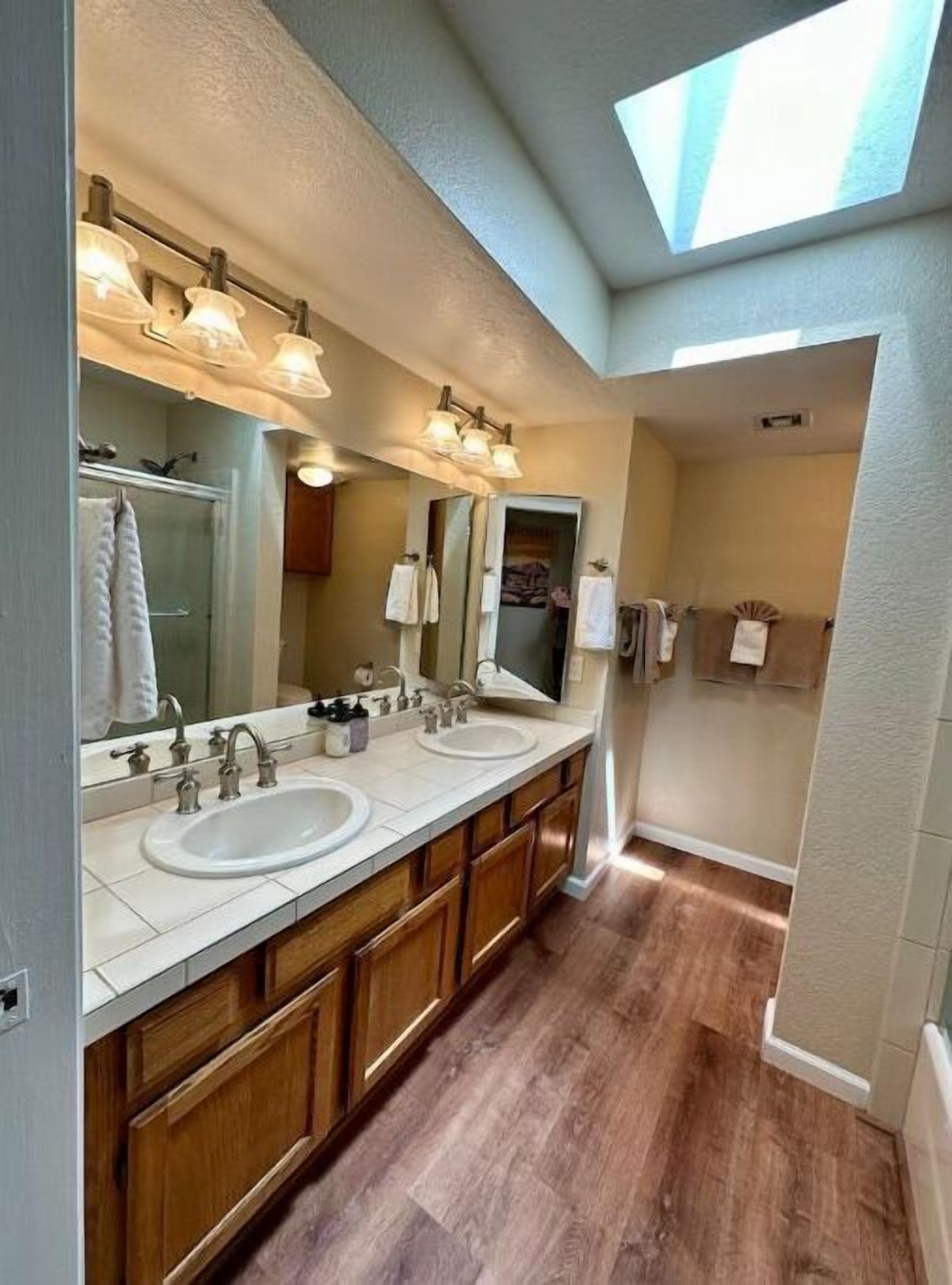 A modern bathroom with a double sink vanity, wooden cabinetry, and a skylight.