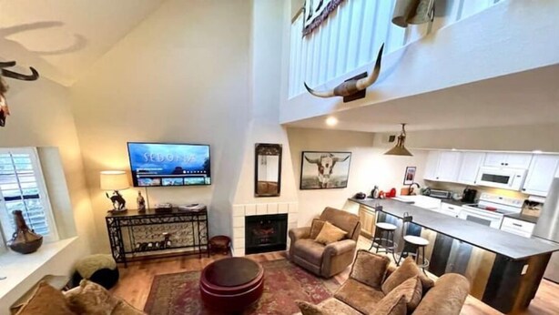 Tilava olohuone, jossa on takka, televisio ja taustalla näkyvä keittiö.