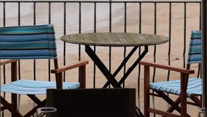 Ein Balkon mit Tisch und Stühlen mit Blick auf einen Strand und grüne Hügel.