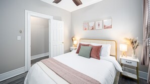 Ein Schlafzimmer mit einem Bett, Nachttischen, einem Deckenventilator und Kunstwerken an der Wand.