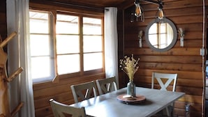Interno di una baita in legno con un tavolo da pranzo, sedie, un vaso con fiori secchi e uno specchio rotondo appeso al muro.