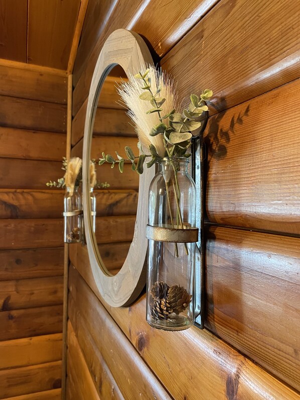 A wooden wall with a mirror and two glass vases with dried plants and pinecones. - JD CABIN!! (Ruidoso)