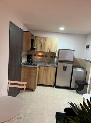 A compact kitchen with wooden cabinets, a refrigerator, a sink, and a dining area with a table and chairs.