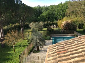Une piscine entourée d’une terrasse en bois et d’une zone herbeuse agrémentée d’arbres et d’arbustes.