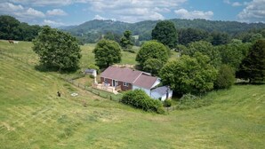 A house surrounded by a grassy field with trees and hills in the background. - Blue Ridge Mountain Getaway (Galax)