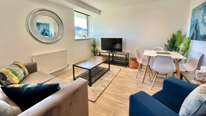Ein modernes Wohnzimmer mit Sofa, Couchtisch, Fernseher und einem Essbereich mit Stühlen und Tisch.