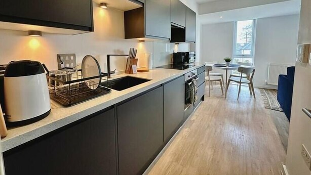 Een moderne keuken met donkere kastjes, een inbouwoven en een eethoek met een tafel en stoelen.
