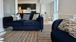 Een moderne woonkamer met een donkerblauwe bank, decoratieve kussens en een vloerkleed met een structuur.