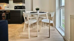 Een moderne keuken met donkere kastjes, een magnetron en een koffiezetapparaat. Er is een eethoek met een witte tafel en stoelen, en een raam met uitzicht op het omliggende landschap.