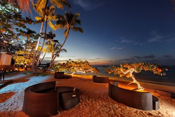Un lounge frente al mar con mobiliario de mimbre y vista al océano al atardecer.