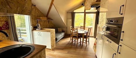Una cocina moderna con armarios de madera, un comedor con mesa y sillas, y un amplio ventanal que proporciona luz natural.