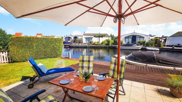 A patio with a table set for two, overlooking a canal with boats and houses. - 2 bedroom nice home in Lemmer (Lemmer)