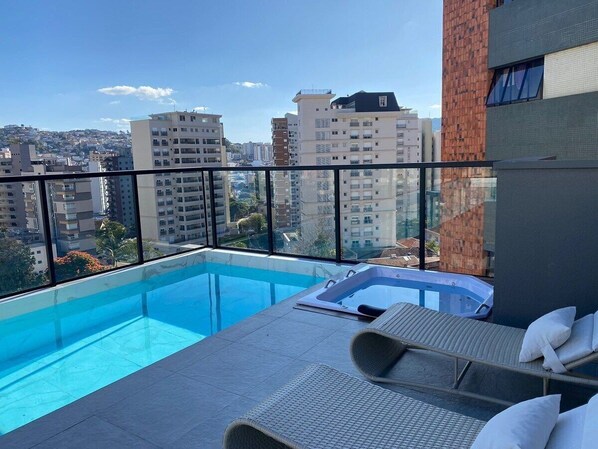 A rooftop pool with a hot tub, lounge chairs, and a city view. - Studio Centro Poços - Tudo a Pe (Poços de Caldas)