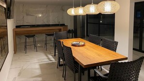 Un comedor moderno con una mesa de madera y sillas negras, una cocina al fondo y un ventanal grande.