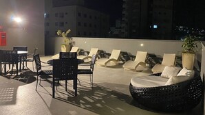 Un espacio al aire libre con sillones reclinables y mesas, rodeado de edificios altos.