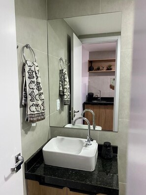 A bathroom with a white sink, a mirror, and two towels hanging on hooks. - Studio Centro Poços - Tudo a Pe (Poços de Caldas)