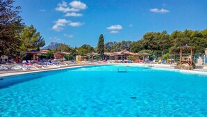 Ein klares, blaues Schwimmbecken mit Liegestühlen und Sonnenschirmen, umgeben von Bäumen und Gebäuden.