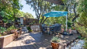 Eine Terrasse im Freien mit Holzdeck, Steinmauern und verschiedenen Kübelpflanzen.