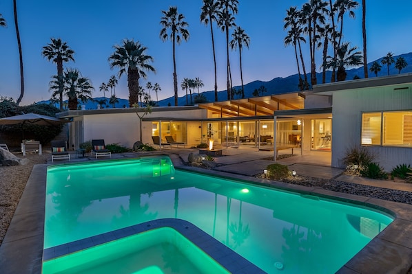 A modern house with a swimming pool, outdoor seating, and palm trees.
