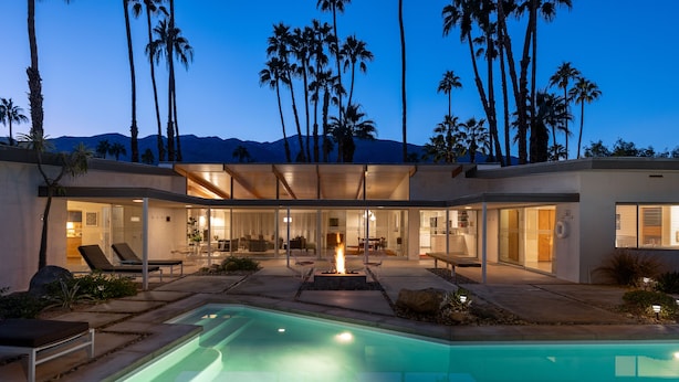 Une maison moderne dotée d’une piscine, d’un espace salon extérieur et d’un foyer.
